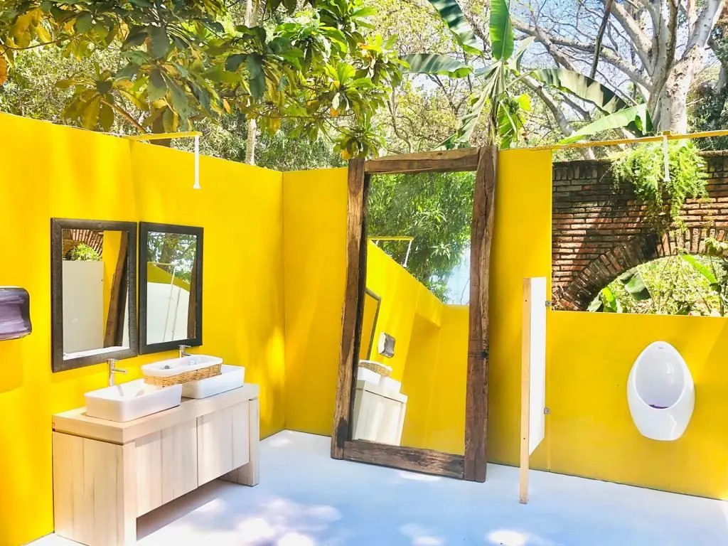 Baño portátil de lujo VIP al aire libre con muros amarillos, tocador de dos lavabos y un espejo grande de marco de madera