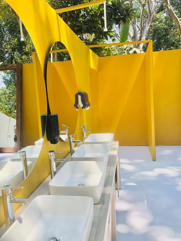 Fila de lavabos blancos con espejo curvo en un baño de lujo al aire libre con muros amarillos