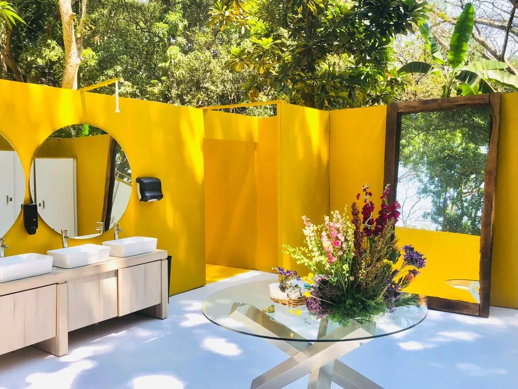 Baño de lujo al aire libre con muros amarillos, espejos y una mesa de flores