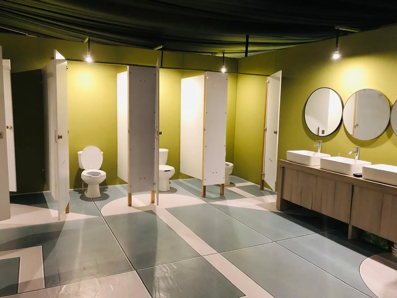 Baño de lujo verde olivo con cubículos y espejos redondos