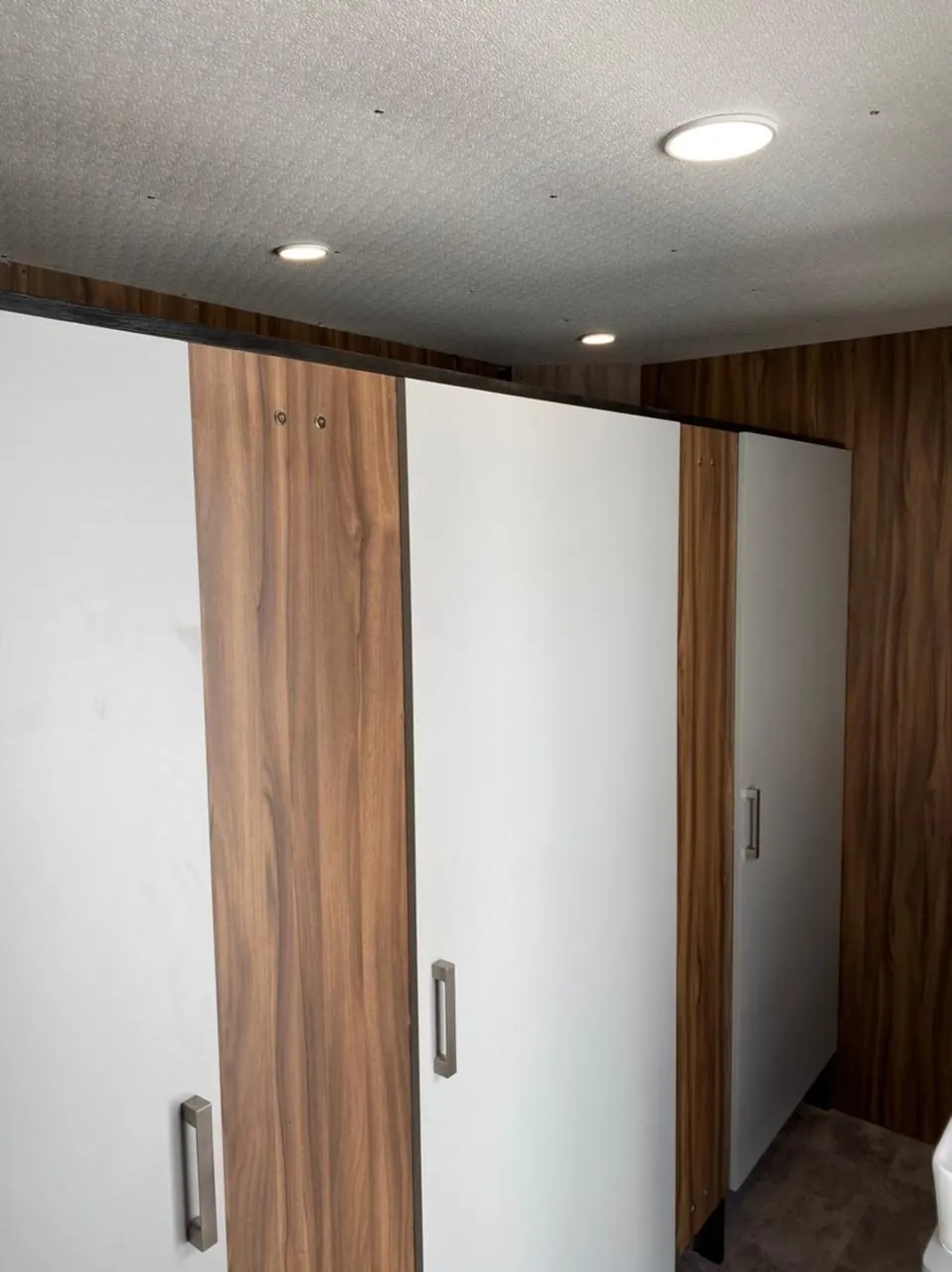 Puertas blancas de los cubículos dentro del baño remolque VIP, con paneles de madera y luz de techo