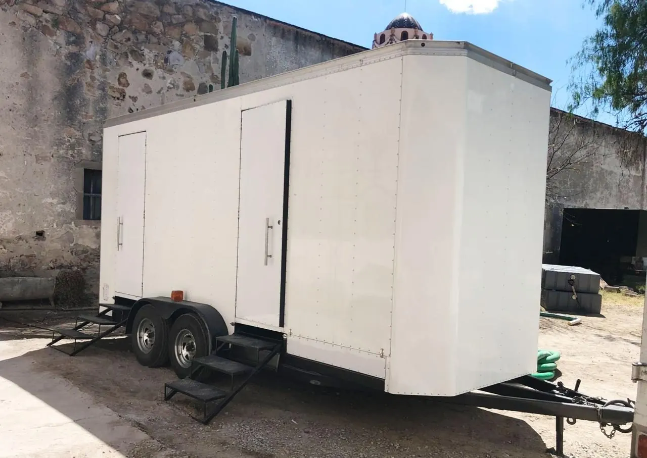 Baño remolque VIP blanco estacionado junto a un muro de piedra antiguo