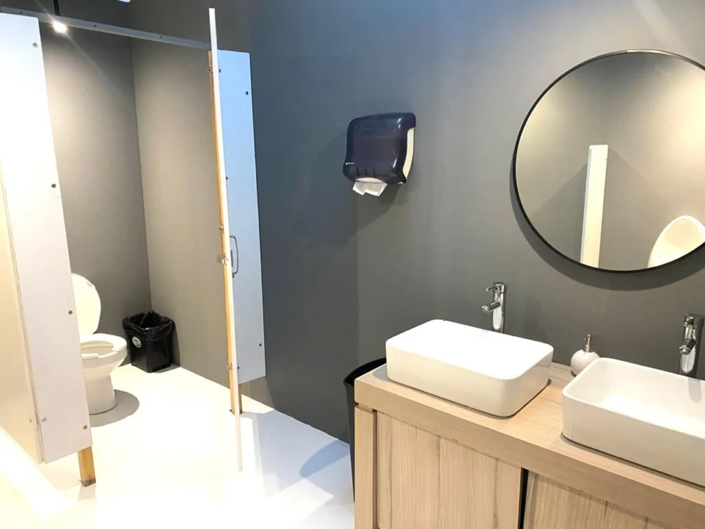 Baño portátil de lujo VIP por dentro: inodoro de porcelana en un cubículo y lavabos blancos con espejo redondo