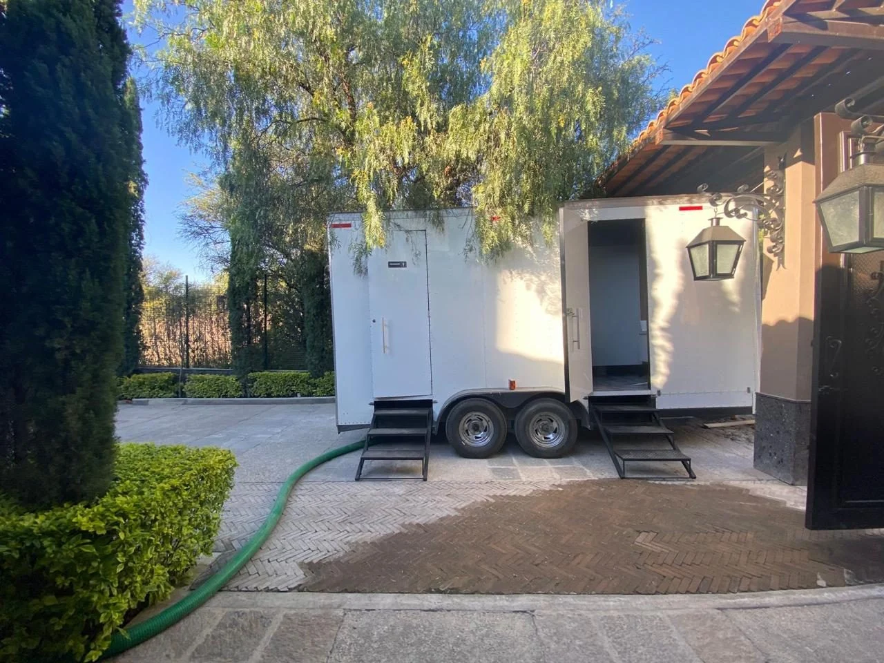 Baño remolque VIP blanco con dos escaleras instalado en el patio de piedra de una hacienda