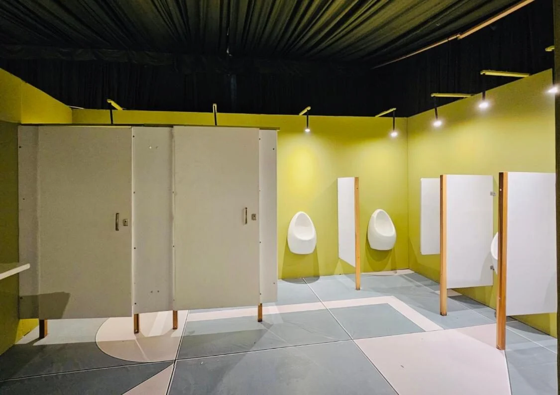 Interior de un baño VIP de Baños VIP con cubículos blancos, mingitorios con divisores y luces de techo