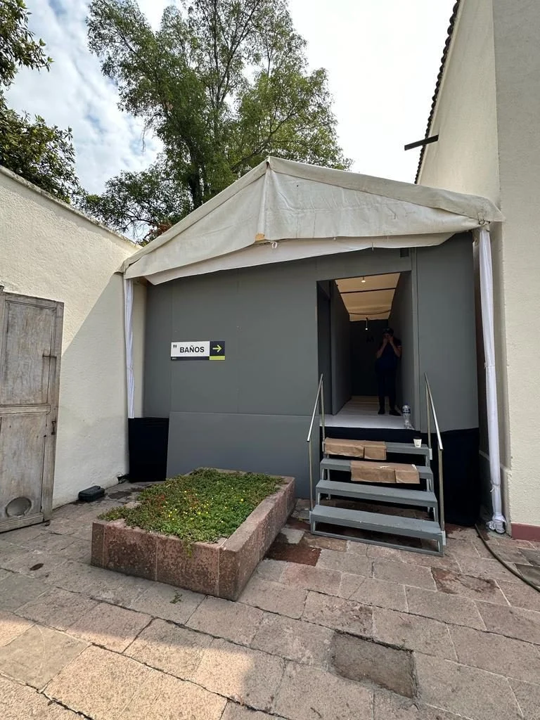 Entrada de un baño portátil de lujo VIP bajo una carpa, con escalera metálica, en un patio de piedra