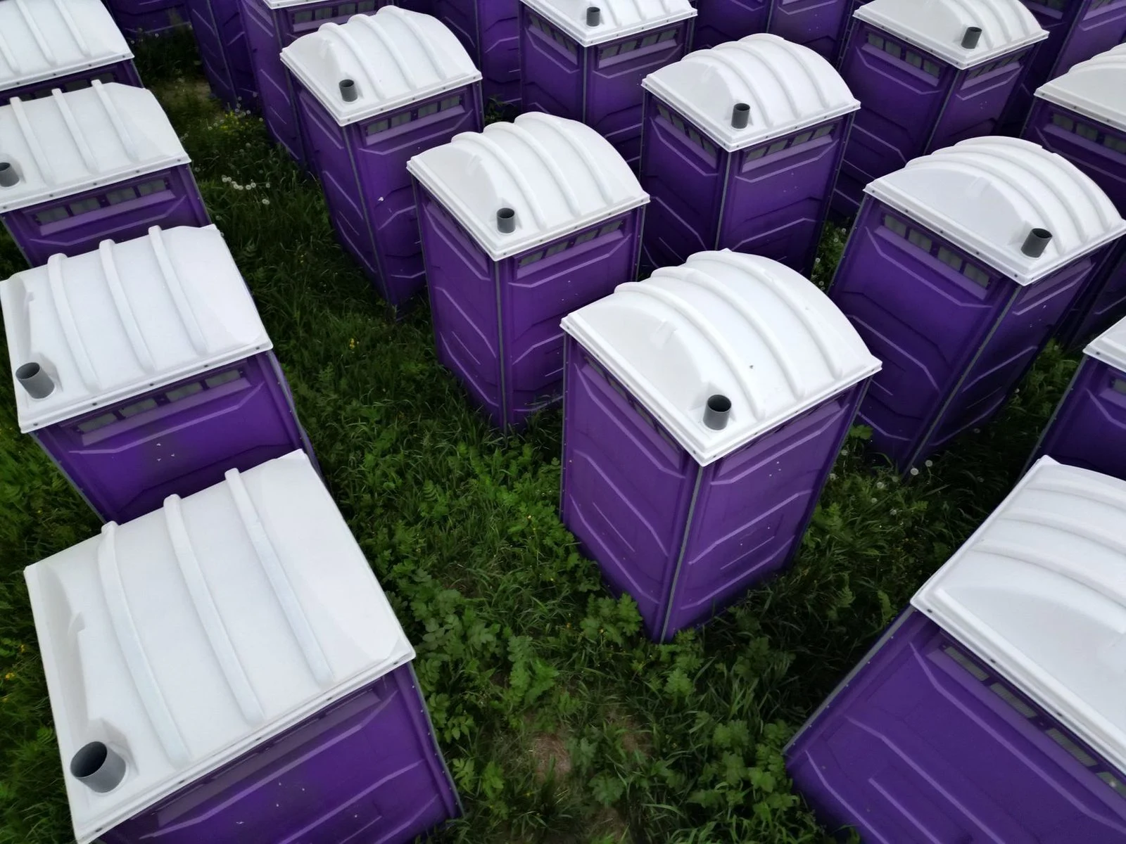 Cabinas portátiles estándar de plástico morado vistas desde arriba sobre pasto